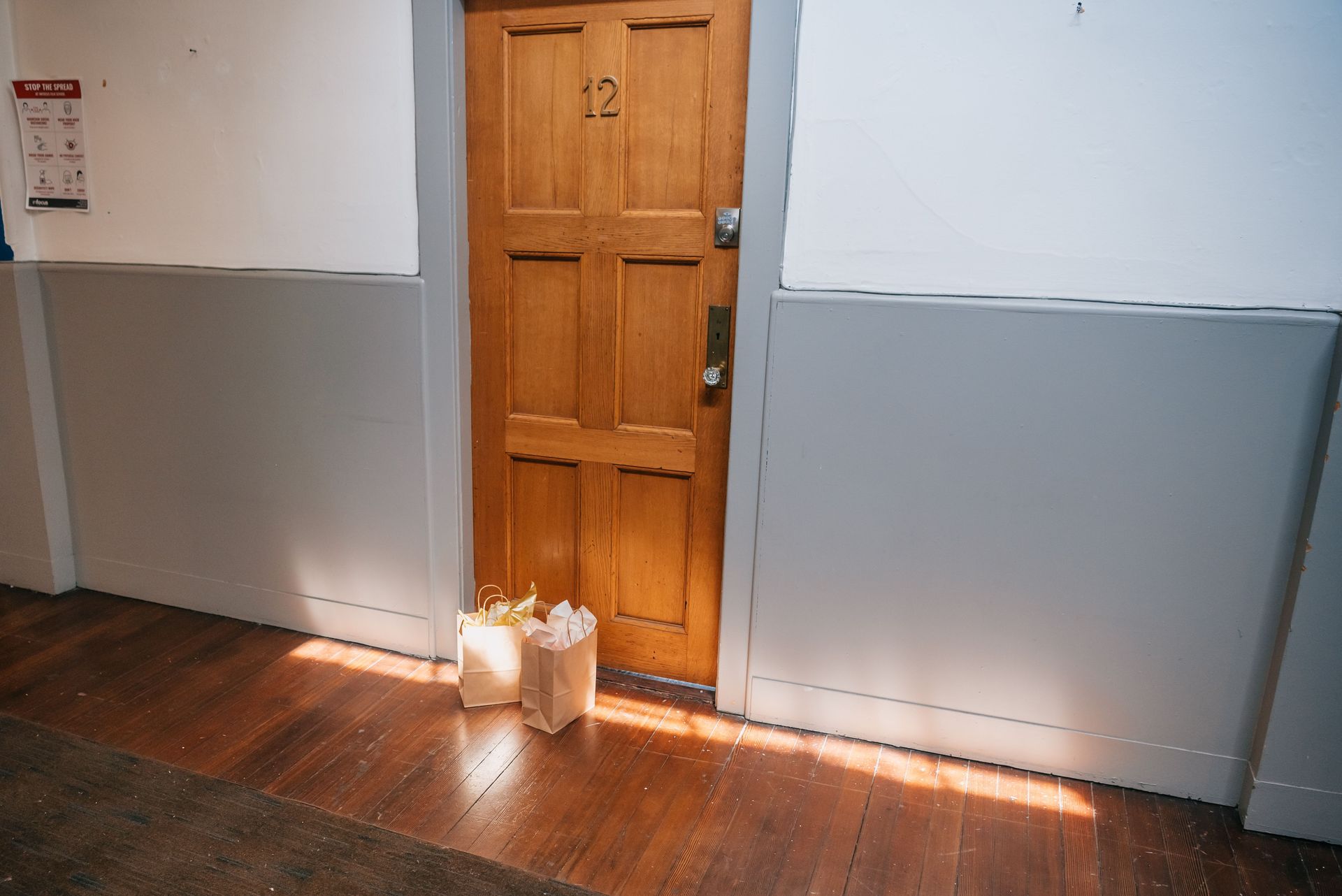 Wooden apartment door with paper shopping bags left outside, basking in warm sunlight.