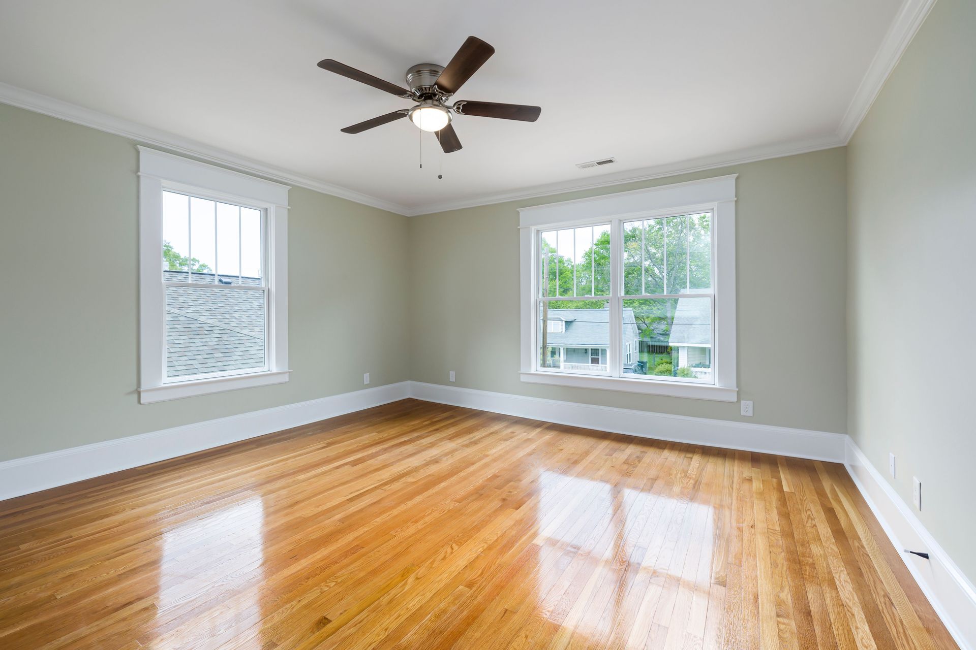 Bright empty room with wooden floors, large windows, and a ceiling fan.