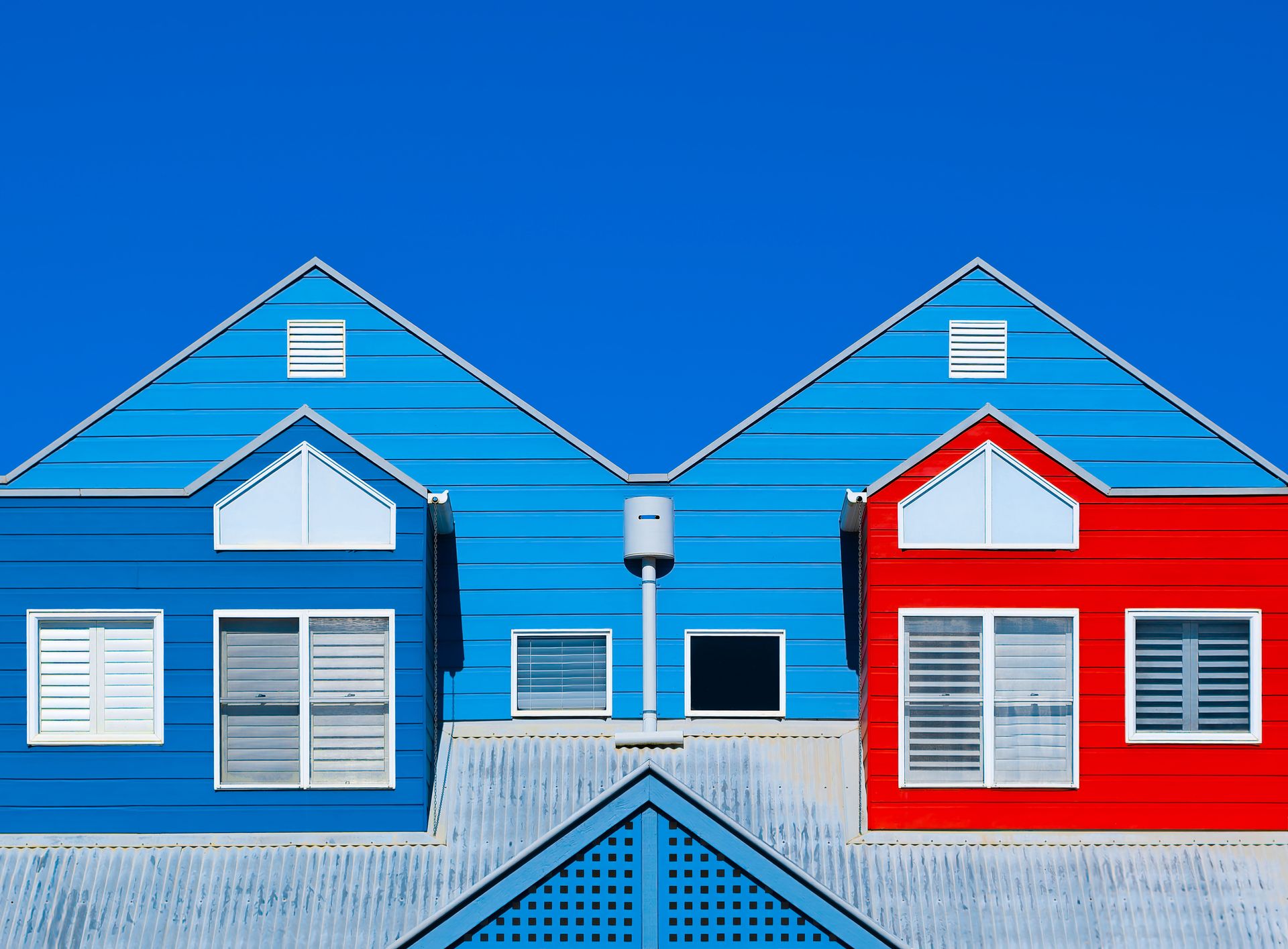 Brightly painted house facades in blue and red create a striking contrast against a clear blue sky.